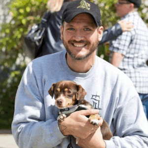 Person smiling, holding a small dog. Rich and George’s first day together outside of OAS in 2014