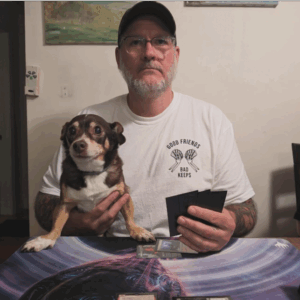 A person holding a small dog. Rich and George playing Magic: The Gathering 11 years later